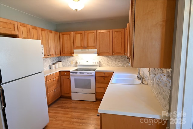 kitchen with backsplash, under cabinet range hood, light countertops, white appliances, and a sink