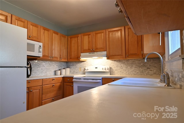 kitchen featuring white appliances, a sink, light countertops, under cabinet range hood, and tasteful backsplash