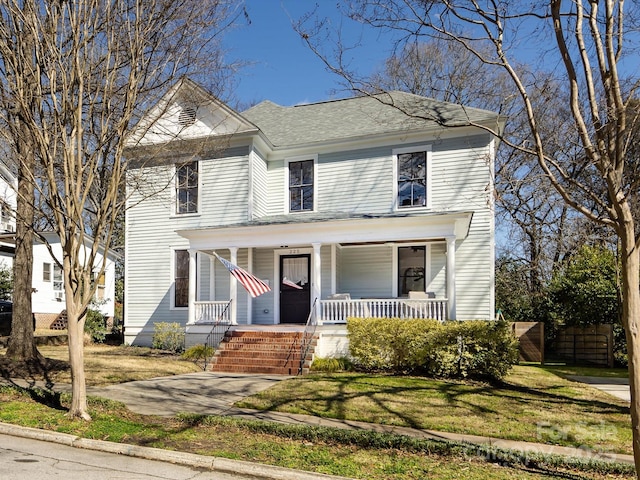 view of front facade with a porch, a front yard, and fence