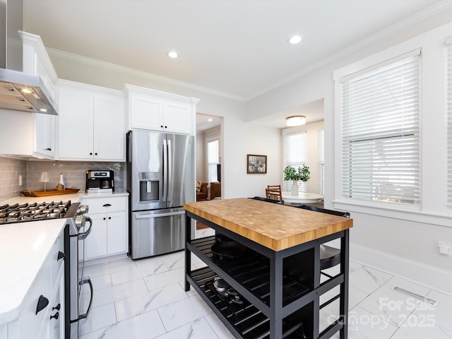 kitchen with backsplash, appliances with stainless steel finishes, ornamental molding, and wall chimney range hood