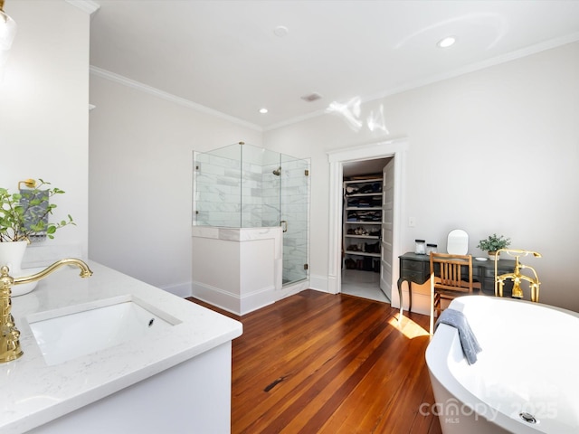 full bath featuring wood finished floors, a soaking tub, a shower stall, a spacious closet, and crown molding