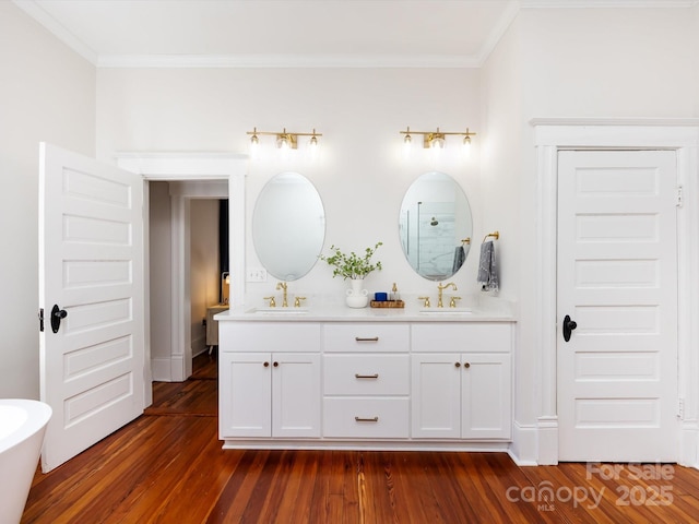 full bath featuring a sink, wood finished floors, double vanity, and ornamental molding