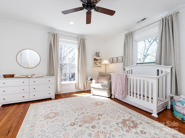 bedroom featuring visible vents, multiple windows, a crib, and ornamental molding