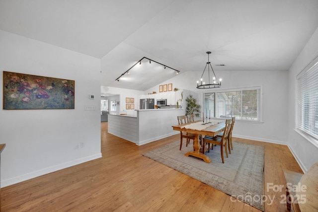 dining room with light wood-type flooring, lofted ceiling, track lighting, an inviting chandelier, and baseboards