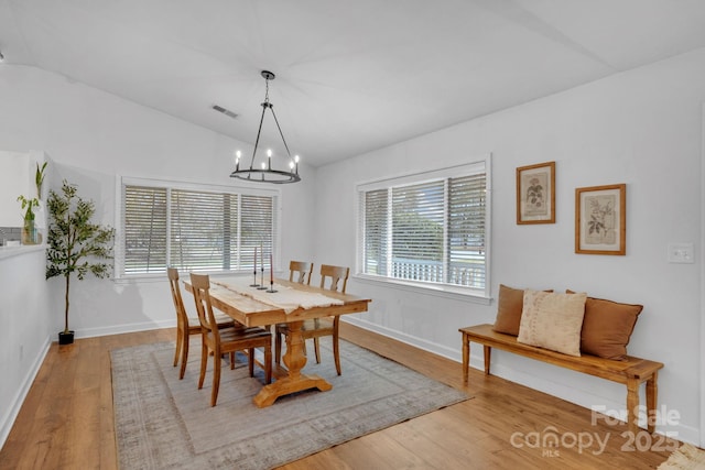 dining space featuring a wealth of natural light, wood finished floors, a chandelier, and vaulted ceiling