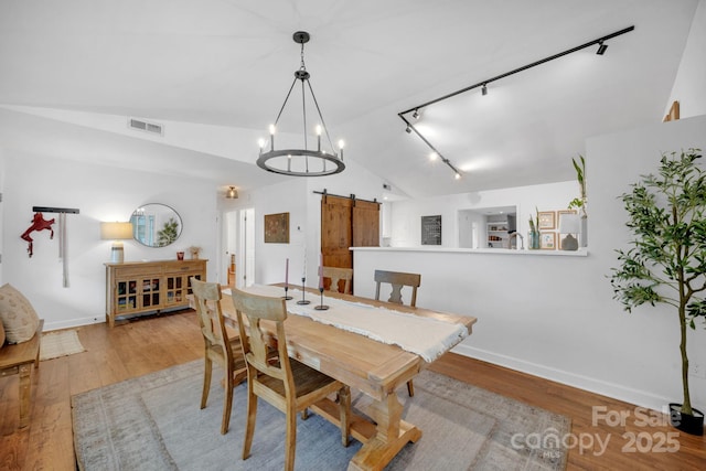 dining space featuring visible vents, a barn door, vaulted ceiling, rail lighting, and wood finished floors