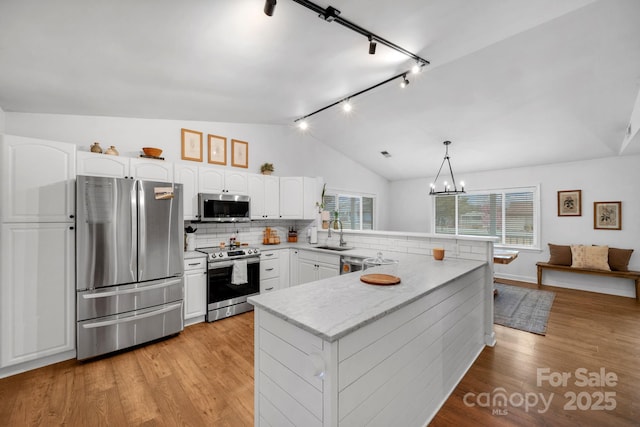 kitchen featuring a sink, stainless steel appliances, a peninsula, light wood finished floors, and lofted ceiling