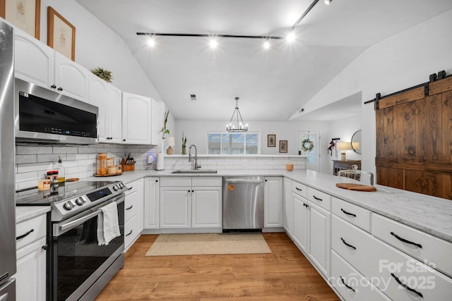 kitchen featuring lofted ceiling, light wood-style flooring, a sink, appliances with stainless steel finishes, and a barn door