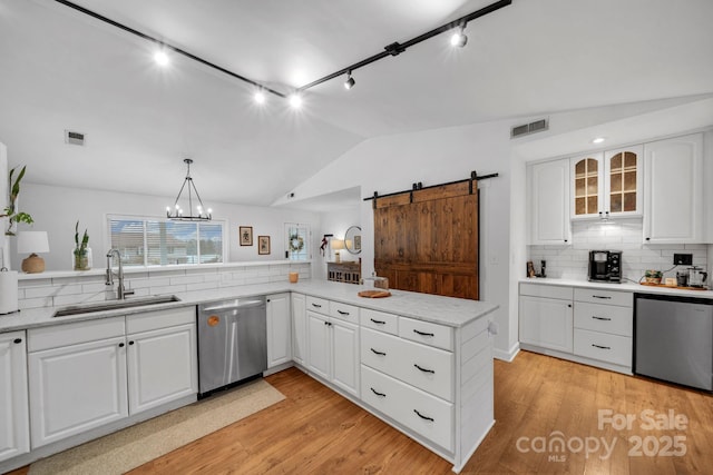 kitchen featuring visible vents, a sink, stainless steel dishwasher, a barn door, and lofted ceiling