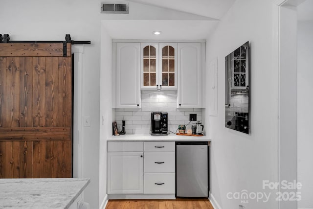 bar featuring visible vents, tasteful backsplash, refrigerator, a barn door, and lofted ceiling