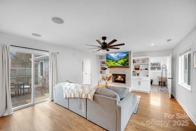 living area featuring a fireplace, light wood-style floors, visible vents, and a ceiling fan