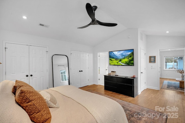 bedroom featuring visible vents, baseboards, multiple closets, lofted ceiling, and wood finished floors