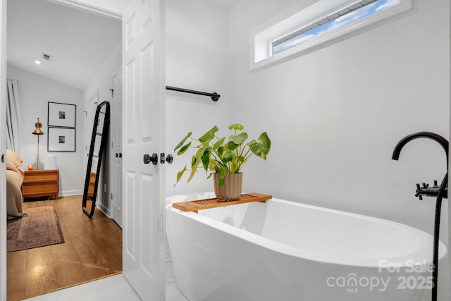 bathroom with lofted ceiling, a freestanding tub, and wood finished floors