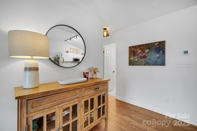 hall with vaulted ceiling, rail lighting, wood finished floors, and baseboards