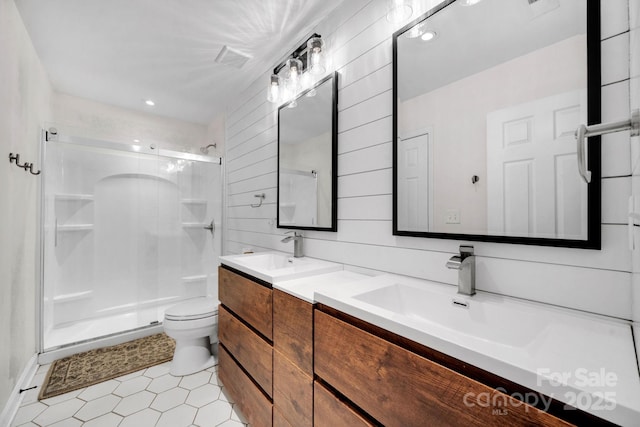 bathroom featuring toilet, a sink, wooden walls, a shower stall, and double vanity