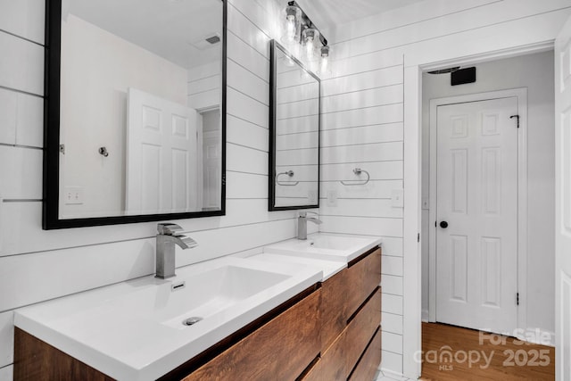 full bathroom featuring double vanity, visible vents, wood walls, and a sink