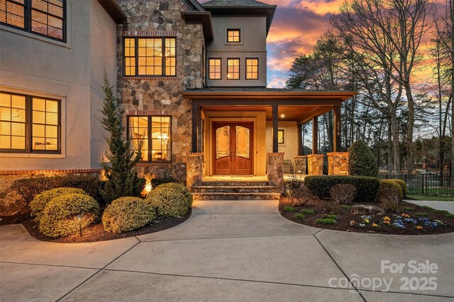 entrance to property featuring stucco siding, stone siding, covered porch, and fence