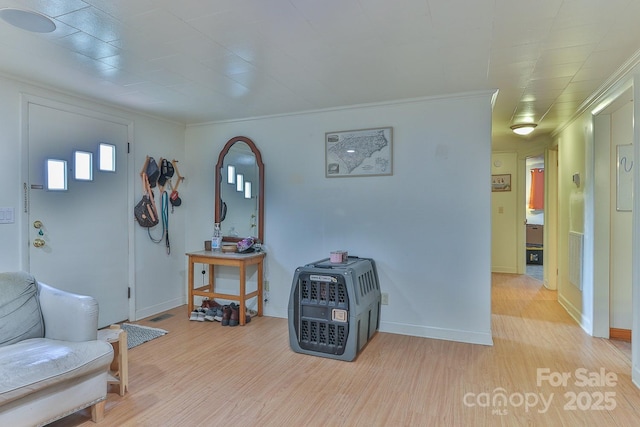 living area featuring visible vents, baseboards, crown molding, and light wood-style floors