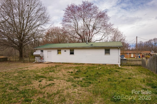 back of property featuring a lawn, metal roof, and a fenced backyard