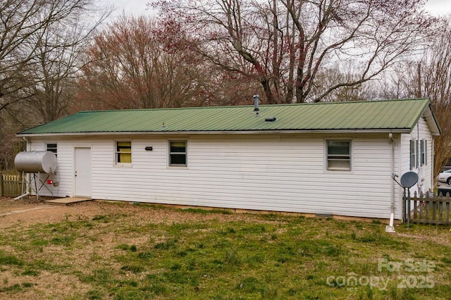 view of side of property with metal roof, a yard, heating fuel, and fence