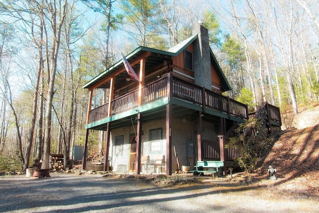 view of front facade featuring a wooded view, a porch, and a chimney