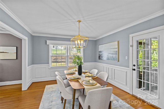 dining space with a wainscoted wall, light wood-style flooring, an inviting chandelier, and ornamental molding