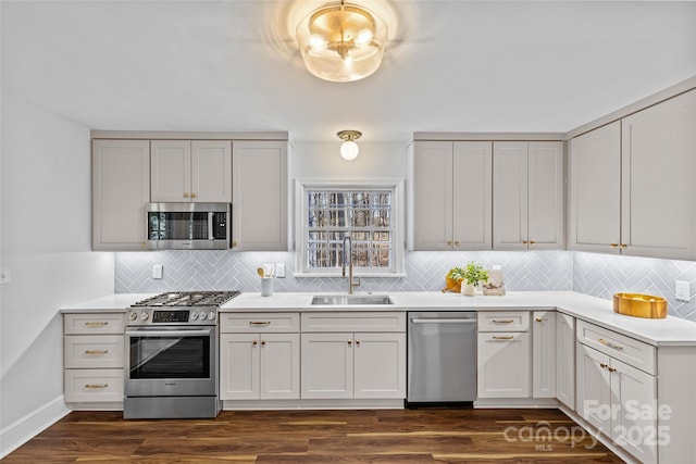 kitchen with a sink, stainless steel appliances, light countertops, decorative backsplash, and dark wood-style flooring