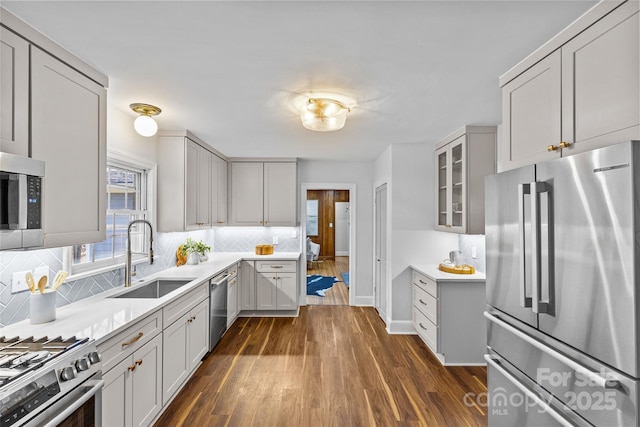 kitchen with glass insert cabinets, decorative backsplash, appliances with stainless steel finishes, dark wood-style floors, and a sink