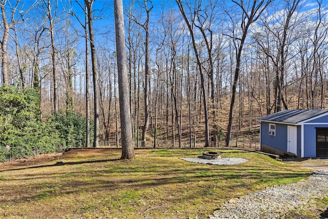 view of yard featuring an outbuilding, a wooded view, and an outdoor fire pit