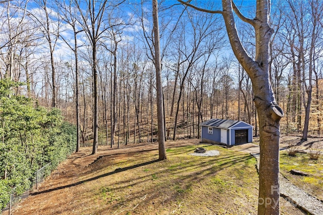 view of yard featuring an outdoor structure, a wooded view, and an outdoor fire pit