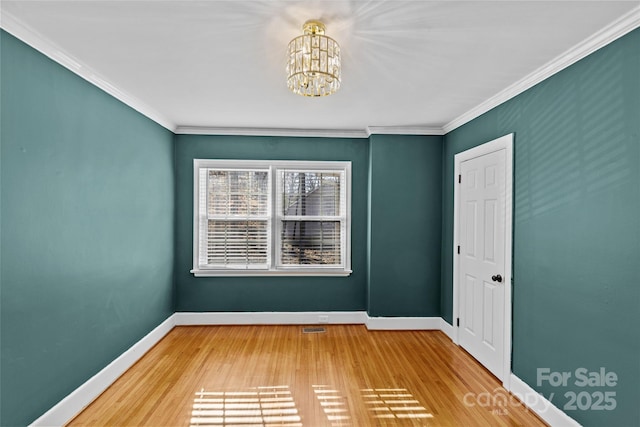 spare room with an inviting chandelier, wood finished floors, crown molding, and baseboards