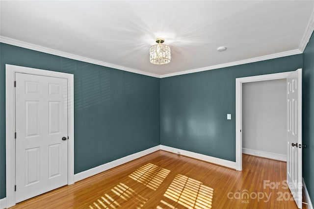 unfurnished room featuring baseboards, an inviting chandelier, wood finished floors, and crown molding