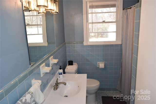 bathroom featuring toilet, curtained shower, tile walls, wainscoting, and vanity