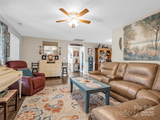 living area featuring a ceiling fan, visible vents, dark wood-style flooring, and a textured ceiling