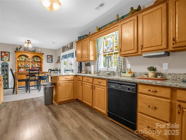 kitchen featuring visible vents, light wood-style flooring, a sink, black dishwasher, and a peninsula