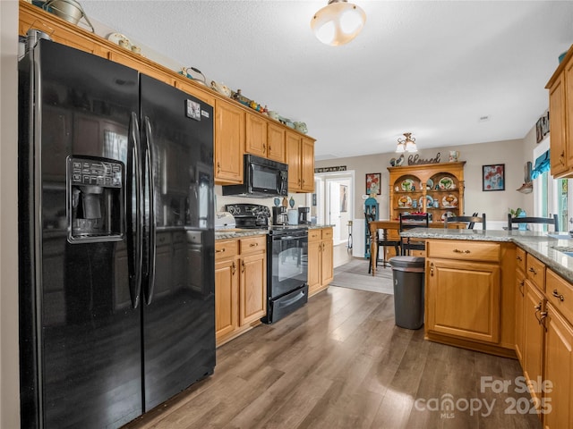 kitchen featuring black appliances, light stone counters, a textured ceiling, wood finished floors, and a peninsula