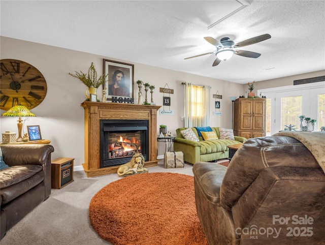 living area with light carpet, a textured ceiling, a glass covered fireplace, baseboards, and attic access