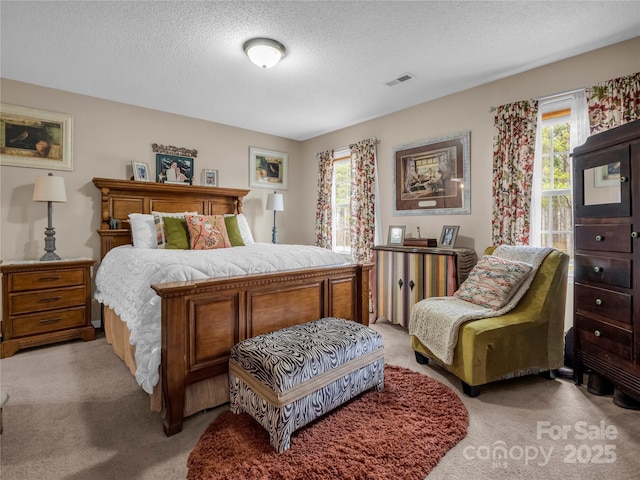 bedroom featuring a textured ceiling, multiple windows, visible vents, and light carpet