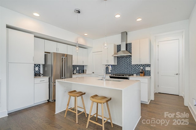 kitchen with freestanding refrigerator, wall chimney range hood, dark wood-style flooring, and a sink