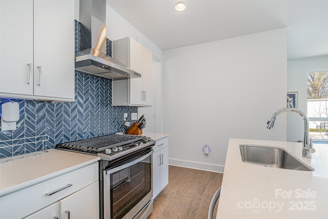 kitchen featuring wall chimney exhaust hood, a sink, light wood-style floors, light countertops, and stainless steel gas range oven