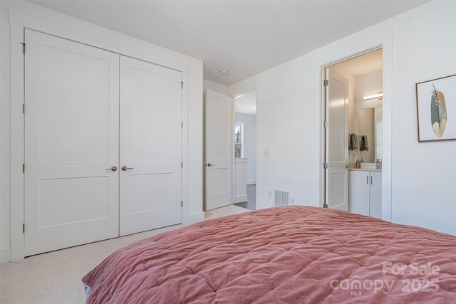 carpeted bedroom with a closet, visible vents, and ensuite bathroom