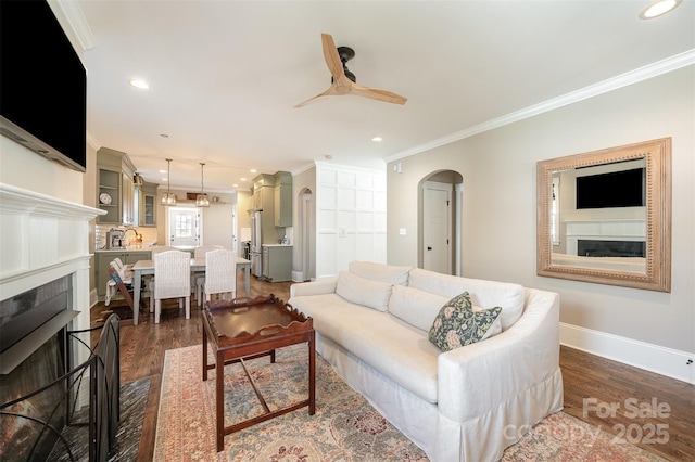 living area with arched walkways, dark wood-style flooring, a fireplace, and crown molding