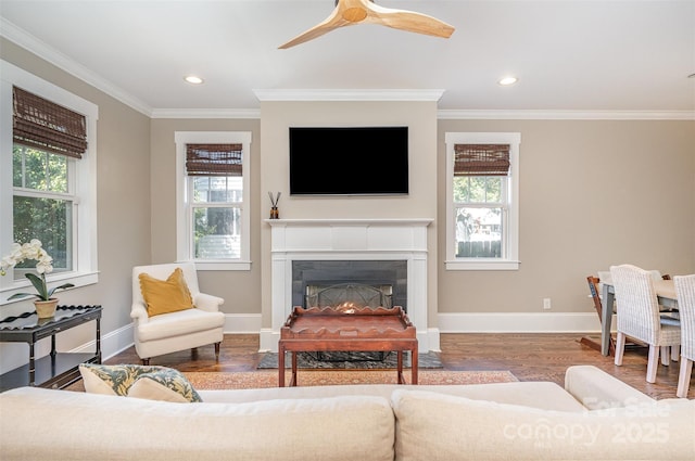 living area with crown molding, baseboards, a lit fireplace, recessed lighting, and wood finished floors