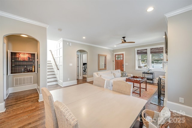 dining room featuring arched walkways, visible vents, ornamental molding, and wood finished floors