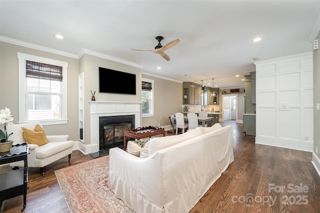 living room featuring dark wood finished floors, crown molding, a fireplace with flush hearth, and recessed lighting