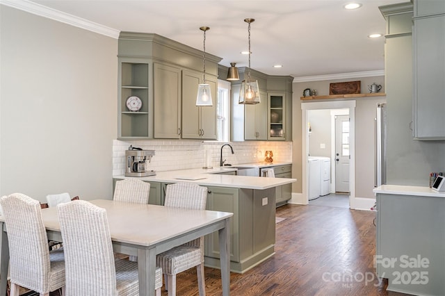 kitchen featuring backsplash, a peninsula, green cabinets, crown molding, and washing machine and clothes dryer