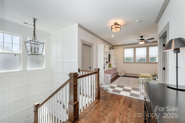 hall featuring visible vents, crown molding, dark wood finished floors, an upstairs landing, and a decorative wall