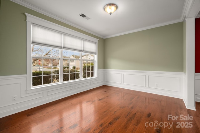 unfurnished room featuring visible vents, crown molding, a wainscoted wall, and wood-type flooring