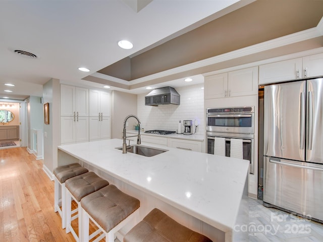 kitchen featuring visible vents, a sink, white cabinetry, appliances with stainless steel finishes, and wall chimney range hood