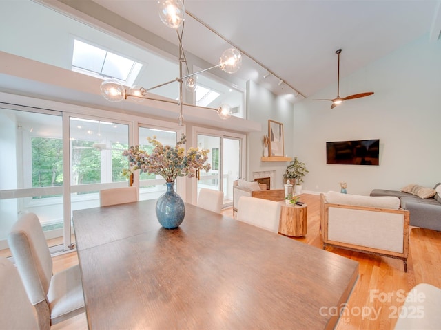 dining space featuring track lighting, light wood-type flooring, a fireplace, a skylight, and high vaulted ceiling